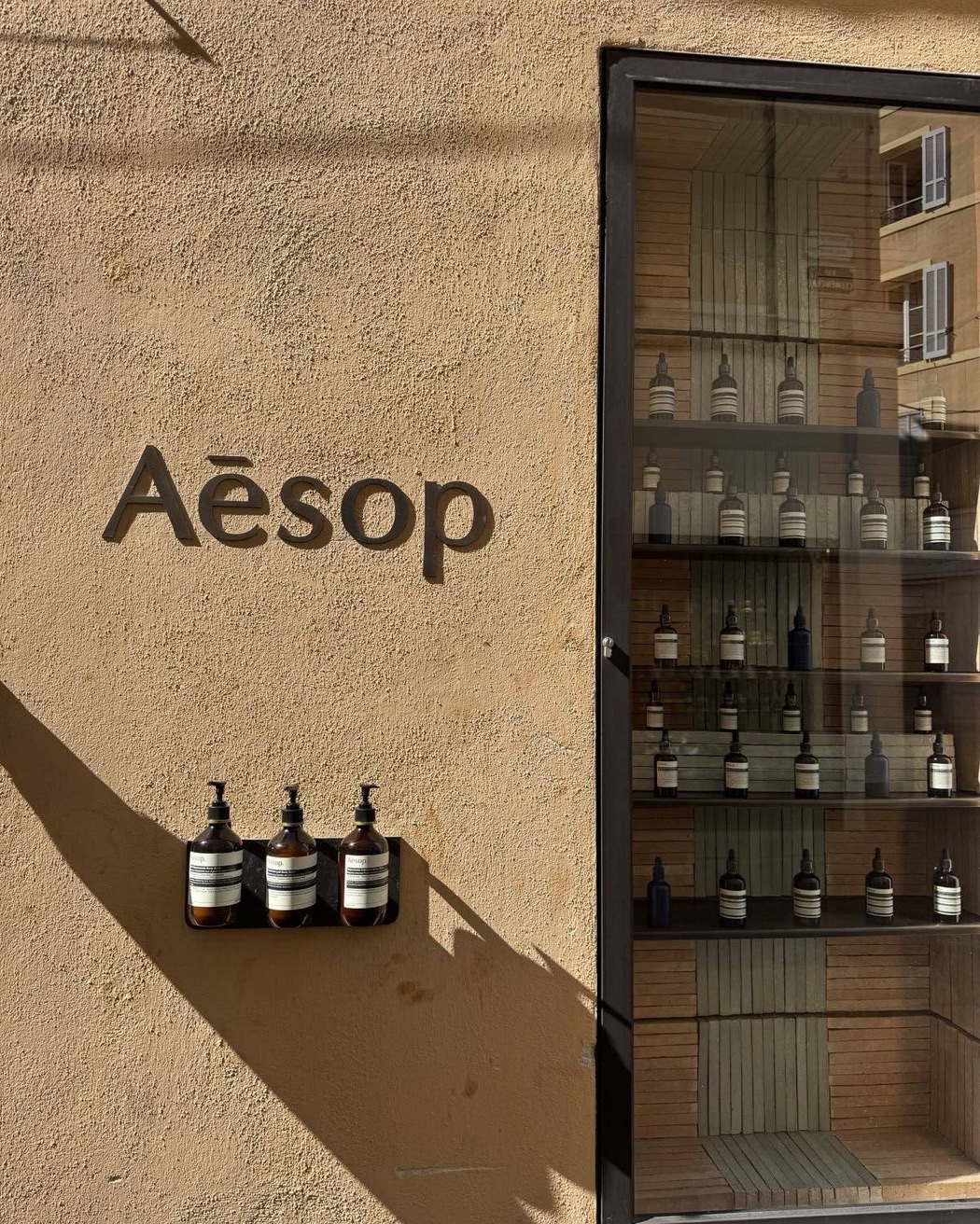 Логотип Aesop на солнечной охристой стене рядом с витриной
