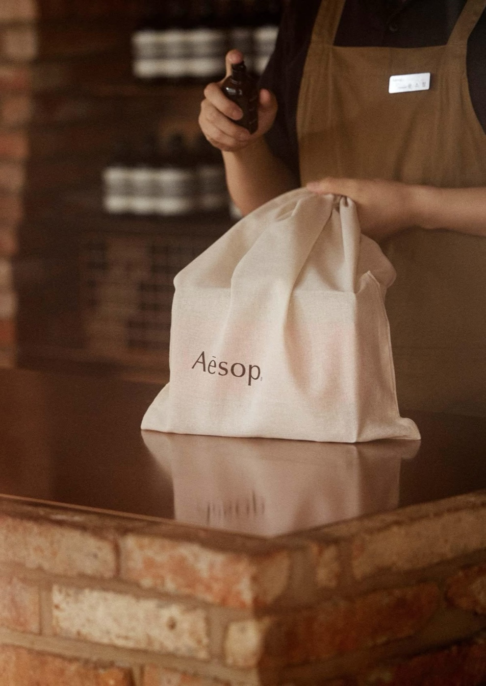 Сотрудник Aesop упаковывает покупку в льняной мешочек