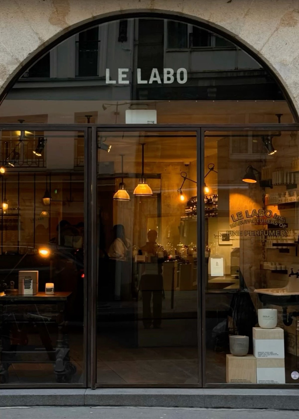 Витрина бутика Le Labo вечером, внутри тёплый свет и полки с флаконами